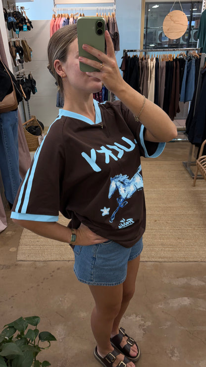 By Frankie Lucky Horse Oversized T-Shirt Chocolate & Blue is a statement everyday tee featuring a bold lucky horse graphic across the bust and a relaxed boxy oversized fit. Designed with a small V-neckline and contrast ribbed edging on the cuffs and neckline, this tee adds a sporty vintage-inspired touch while keeping your look comfortable and effortless.