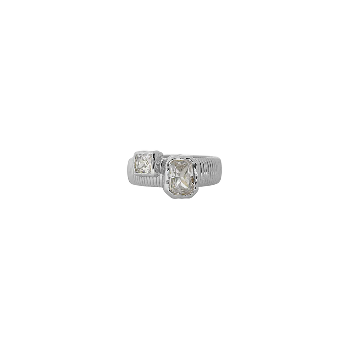 Sculptural and serene, the Maia Ring in silver brings together ancient influence and modern clarity. Its ribbed circular band is crafted in a cool silver-tone finish, framing two rectangular cubic zirconia stones in molten-textured bezel settings—subtle sparkles that evoke the shimmer of starlight on water.