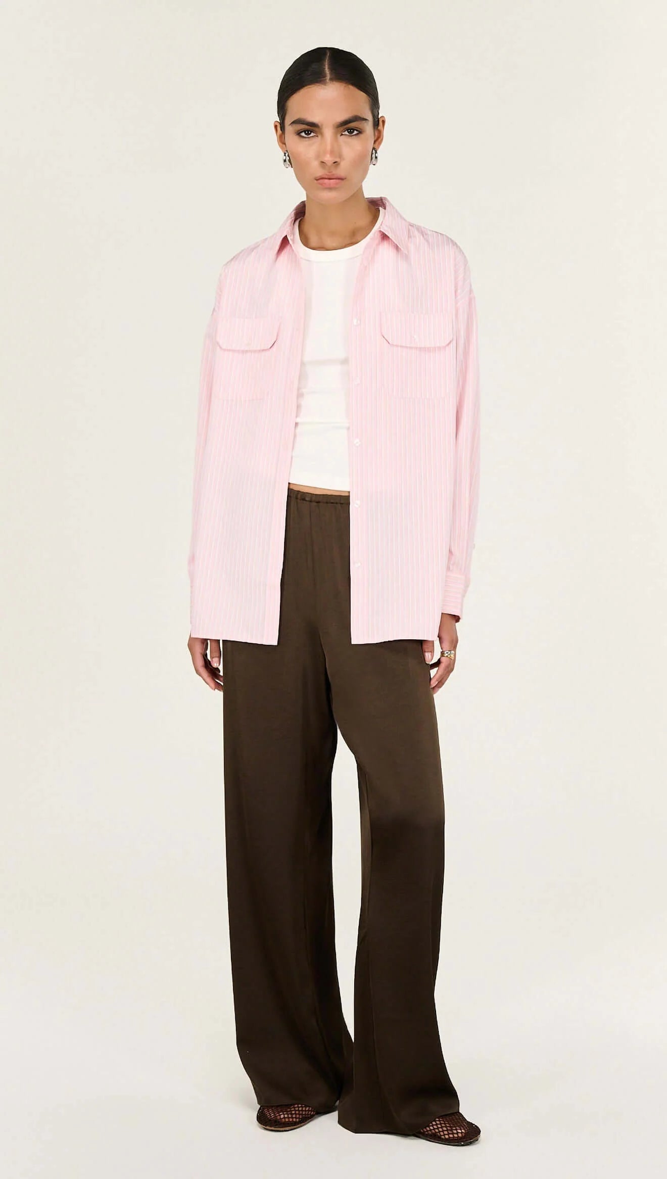 The Lina Pink Pinstriped Shirt is a modern wardrobe essential designed with a relaxed silhouette and timeless shirting details for effortless everyday wear. Crafted from a lightweight woven fabrication, it features a classic collar, button-through front and soft vertical stripe pattern for a polished yet easy finish.

- Classic collar neckline
- Button-through front closure
- Relaxed, longline silhouette
- Dual front patch pockets
- Soft pink with fine stripe detailing
- Lightweight, breathable feel
- Desig