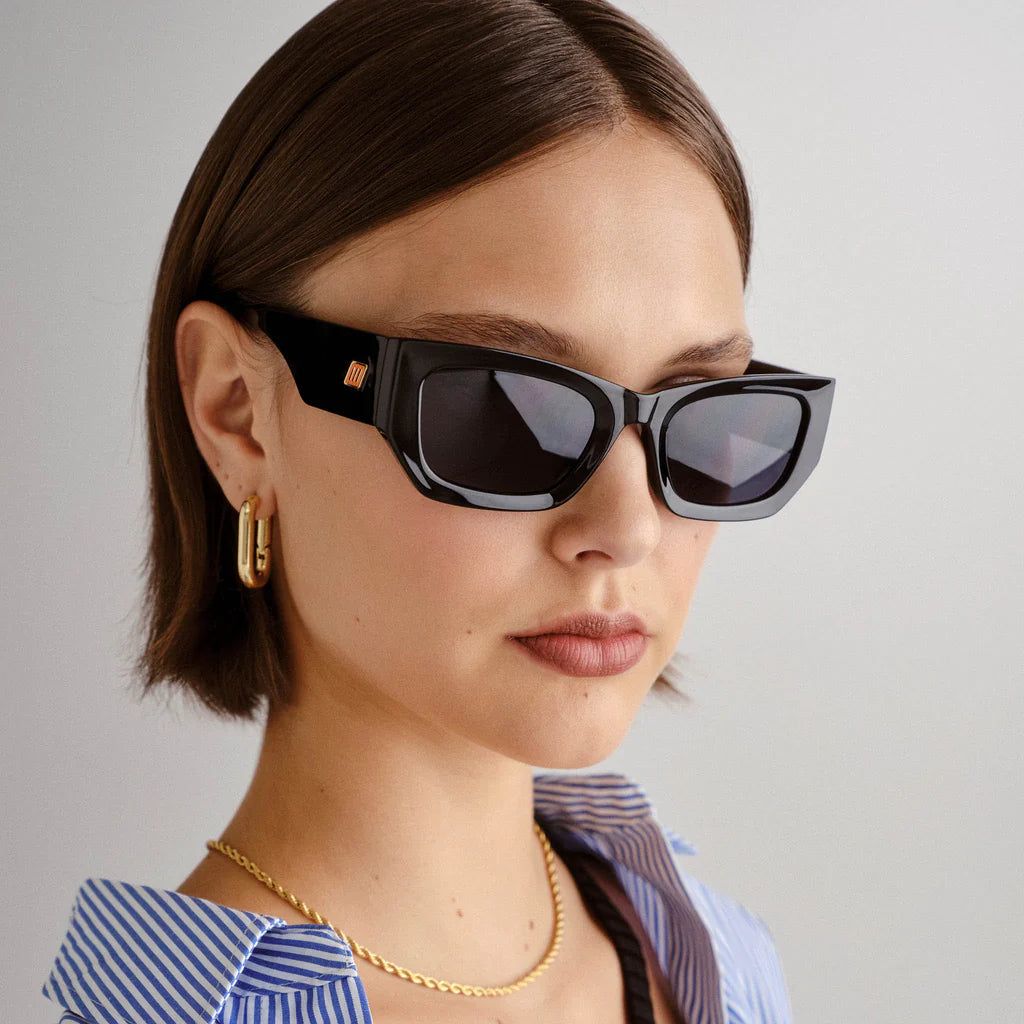 Timelessly elegant and sophisticated, our BEACHCOMBER sunglasses are an everyday staple. Featuring a low bridge fit, bold edges and bevelled lines, this frame is finished with a square flagstripe hardware with custom enamel fill to each temple.

• Finished in shiny black with bright gold hardware and dark tonal lenses for a sleek look.
• Made using BPA free polymer plastic which is lightweight, durable and impact resistant
• Fitted with shatterproof and scratch resistant polycarbonate lenses.